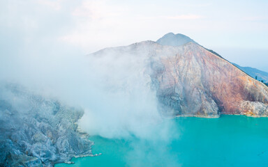 Volcanic landscape at sunrise, a vibrant turquoise sulfur lake and rocky mountains completing the...