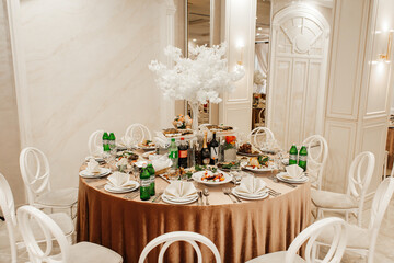 On the table there are dishes with snacks such as cold cuts, grapes and greens. Also on the table are bottles of drinks, glasses and cutlery.