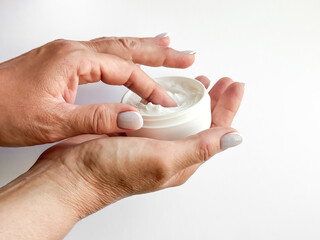 Close up of middle age woman hands holding container of cream and dipping finger on white...