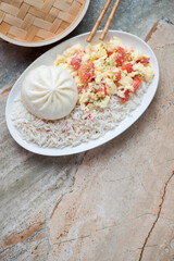 Plate with chinese tomato egg-stir fry, steamed rice and baozi, vertical shot on a grey and roseate granite background with space, high angle view