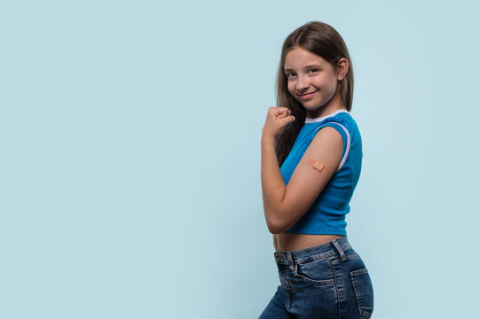 A young girl flexing her arm and showing a bandage after vaccination in a studio, smiling confidently