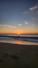 Sunrise with beautiful orange halo contrasting with blue skies and minimal clouds and waves on the beach in Cabo. Pacific Ocean. Serene. View 1. 