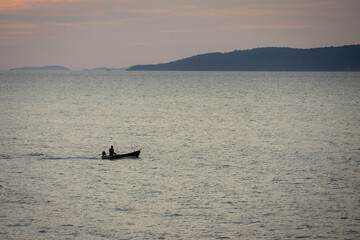 silhouette lone boat cuts through the calm waters as the sun begins its descent, casting a warm glow across the horizon
