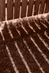 Shadows of a wooden picket fence in a front yard, front garden with grass. Color of the Year 2025 Mocha Mousse color. Chocolate or Brown Background