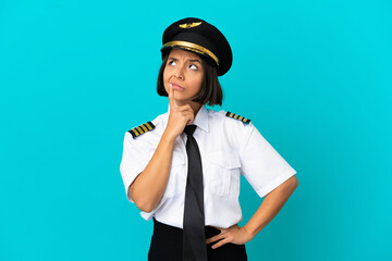 Young airplane pilot over isolated blue background having doubts while looking up