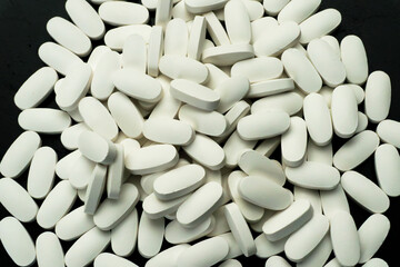 Large quantity of white tablets scattered on a dark surface