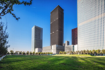 Obraz premium Skyscrapers Towering Over Green Urban Park under Blue Skies