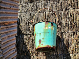Rusty old enamelled bucket with the Dutch text ‘groenten’ (veggies) hanging on a reed fence in...