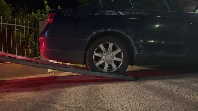 A black damaged car involved in accident is being towed by a tow truck ramp