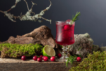 Cranberry cocktail with ice, lime, and rosemary on a old wooden board.