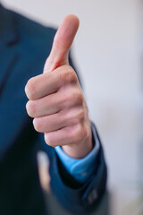 Close-up of a businessman giving a thumbs-up gesture in a suit.Vertical