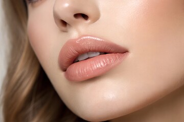 Close-up of a woman's lips with nude glossy lipstick and natural makeup 
