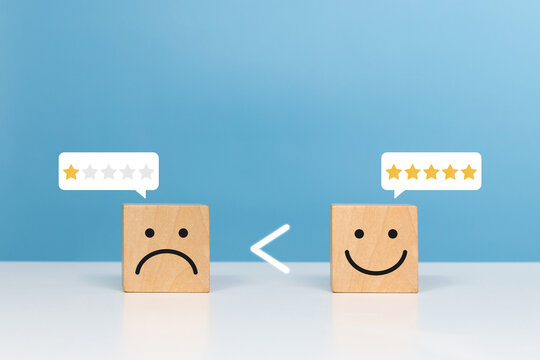 Service rating, optimism, positive, feedback. Wooden block with smile face and greater than sign between bad face emoticon indicates optimism is bigger and better than sadness