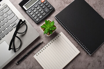 Bookkeeping workplace concept. Top view Calculator, laptop, notebook, pen, glasses and plants on dark gray table