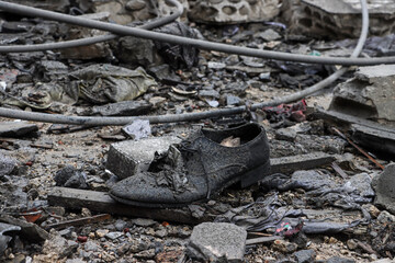 A black shoe amidst rubble and debris in an urban war-torn area, evoking devastation, chaos, and tragic aftermath of destruction and conflict. loss, war, forgotten belongings, tragedy, or resilience
