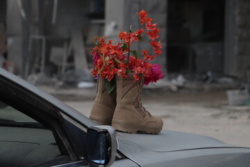 Beige military boots filled with red bougainvillea flowers on a car portraying peace, hope, resilience, martyrdom and the contrast between war and renewal through nature.