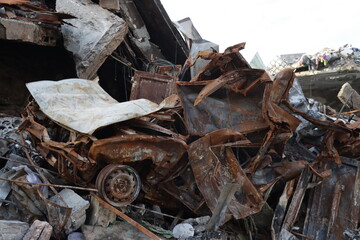 A scene of devastation showing rusted vehicle remains and structural debris, highlighting the aftermath of a disaster in an urban area with ruined architecture.