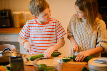 A brother and sister help their mother in the kitchen, chopping mushrooms, cucumbers, and tomatoes....