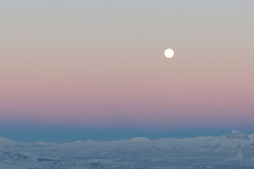 Full moon during sunset with snowy mountains