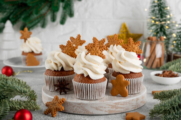 Christmas gingerbread cupcakes with cream cheese frosting and mini gingerbread cookies on top on a wooden board. Festive dessert.