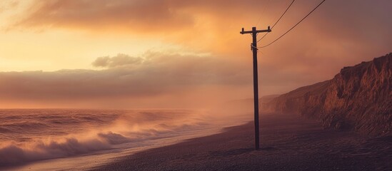 Obraz premium A lone power pole on a beach with a hazy sunset and crashing waves.