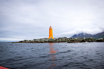 Orange lighthouse standing on rocky island in iceland