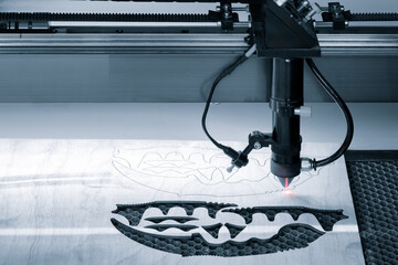 A laser cutter is cutting a design into a piece of wood. The design is a flower