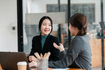 Obraz premium Two women engaged in a business discussion in a modern office, showcasing teamwork and collaboration.