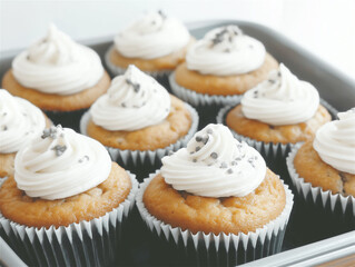 Freshly baked cupcakes with whipped cream topping and sprinkles, displayed on a baking tray, representing home-baking, celebration, and sweetness.