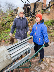 children carry a wheelbarrow with metal, poor children earn money, autumn, mother carries garbage, poor family, burnt house, homeless people