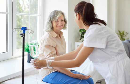 Senior woman with intravenous drip sitting on medical couch, physician, nurse fixing IV drip infusion, geriatrics hospital eldercare, therapy to infuse vitamins, drugs to maintain health in clinic
