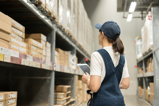 Warehouse worker hands holding tablet check stock on tall shelves in warehouse storage. Asian woman auditor or staff work looking up stock taking inventory in cargo store. Logistic business work.