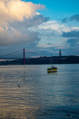 Yellow tour boat sailing on tagus river with 25 de abril bridge and cristo rei statue in background