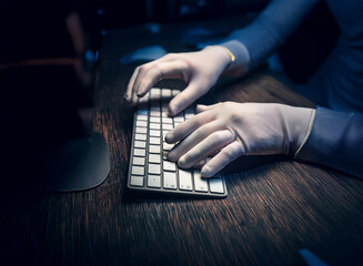 Close-up of gloved hands typing on a keyboard in a dimly lit room.  The scene suggests secrecy or a clandestine operation.