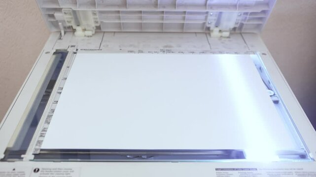An office worker scans an A3 sheet of paper on a scanner. A man's hand presses a button to scan or copy a document on an office MFP.