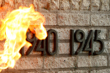 Flames burn above the dates 1940 and 1945, etched into a stone wall.  A memorial?