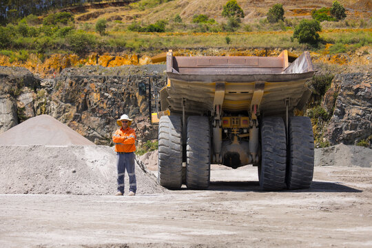 Man with arms crossed standing behind the hauler truck with massive wheels.