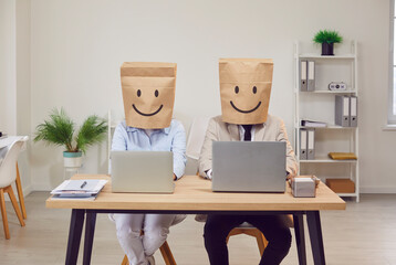 Business people with paper bags on their heads sit at their laptops. Office workers pretend to smile. Concept anonymous office workers, smile drawing, false optimism, unrecognizable