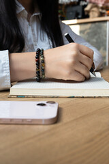 A young girl opens a pen and writes something in a notepad. Girl's hands close-up. In the foreground is a telephone. Side view. Vertical photo. High quality photo