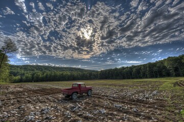 Naklejka premium Open Field Of Freshly Harvested Crops With Vintage Red Pickup Under Cloudy Sky At Sunset