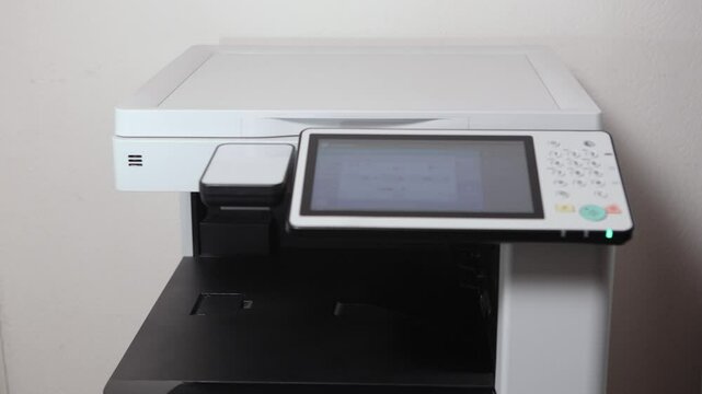 An office worker scans an A3 sheet of paper on a scanner. A man's hand presses a button to scan or copy a document on an office MFP.