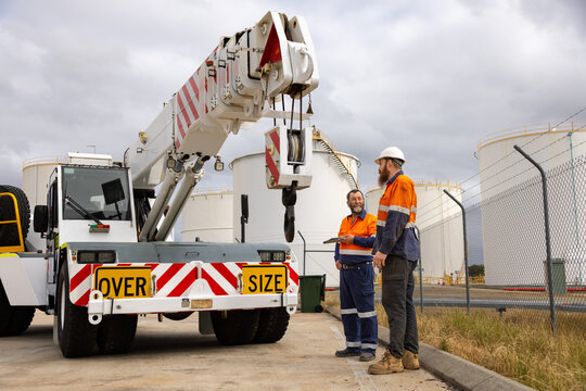 Male workers standing in front of pick and carry franna crane on industrial site