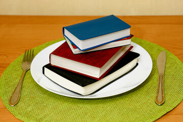 On a napkin on the table next to the whiskey and knife there is a plate with a stack of books., food for the mind