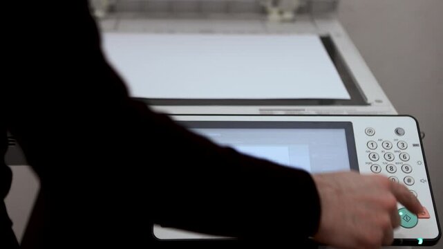 An office worker scans an A3 sheet of paper on a scanner. A man's hand presses a button to scan or copy a document on an office MFP.