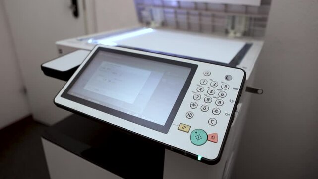 An office worker scans an A3 sheet of paper on a scanner. A man's hand presses a button to scan or copy a document on an office MFP.