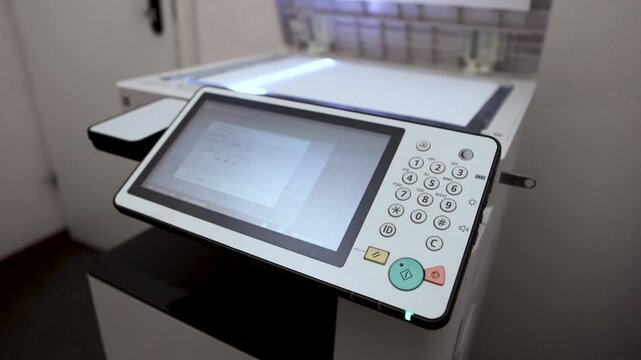 An office worker scans an A3 sheet of paper on a scanner. A man's hand presses a button to scan or copy a document on an office MFP.