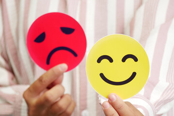 Hands holding a blurred card sad face and happy face. Concept of introversion, bipolar, depression,...