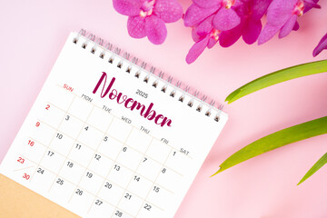 Desk calendar for November 2025 with blooming pink orchid. Flat lay.