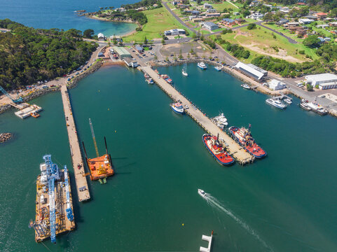Aerial view of boats and cranes alongside long piers in a coastal harbor