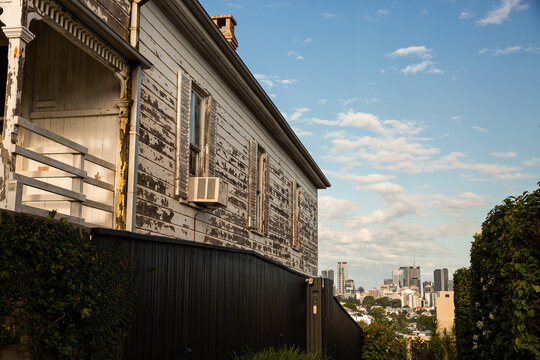 a side of a run down old house with paint peeling and city buildings in the distance
